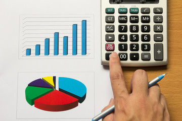 Business man press calculator on financhart and graph with pen,