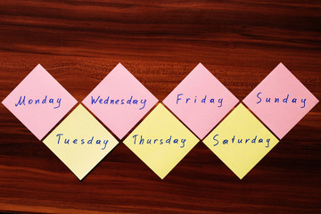 Schedule. Days of the week written on colored notes lie on a wooden table.