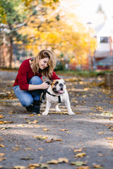 Pretty woman enjoying in park with her adorable English bulldog. Autumn time. 
