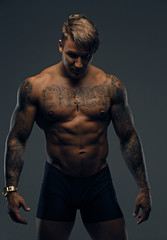 Fototapeta na wymiar Portrait of tattooed muscular male in a shadow.