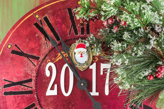 Arriving 2017. Clock decorated with Santa Claus face and fir in snow.