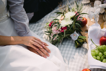 the bride and groom holding hands on a picnic. Bouquet, fruit, candles lying on the blanket