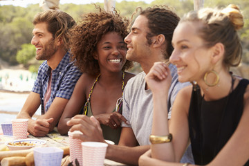 Four friends sit in a row at a table by the sea, close up