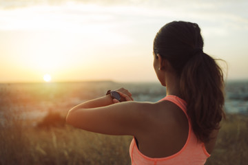 Sportswoman checking running and workout goals on smart watch towards beautiful sunset.