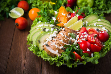 Healthy salad plate with colorful tomatoes, chicken, cheese, avocado, lime and mixed greens on wooden background close up. Food and health. Nutritious meal.