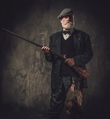 Senior hunter with a shotgun in a traditional shooting clothing, posing on a dark background