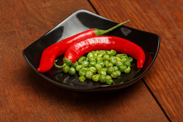 Hot chilli peppers and green crispy peas snacks in ceramic plate