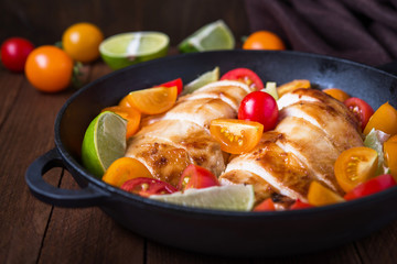 Sliced chicken breasts with colorful cherry tomatoes and lime on dark wooden background close up. Healthy food.