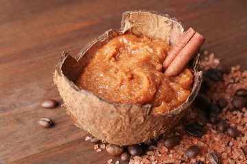 Body scrub with cinnamon stick in coconut shell on wooden background
