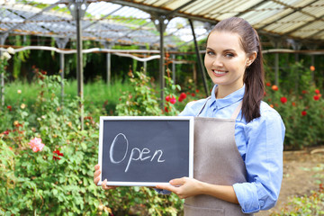 Pretty young gardener holding board with inscription OPEN