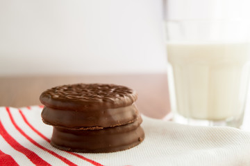 Chocolate cookies on white linen napkin and a glass of milk on w