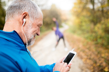 Senior runners in nature, stretching. Man with smartphone with e