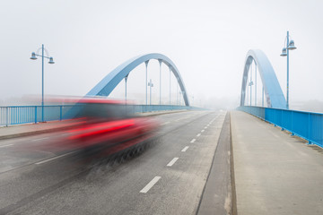 Fototapeta na wymiar Red car crossing a bridge in the fog 