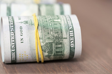 Rolls of one hundred US dollar bills on a wooden table