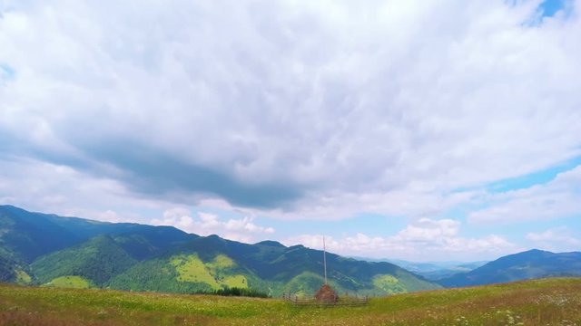 Timelapse of Clouds Passing by Summer Landscape with Haystack on a Foreground and Mountains on the Background. 4K. 
