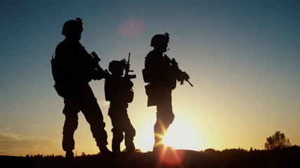Squad of Three Fully Equipped and Armed Soldiers Standing in Desert Environment in Sunset Light. Slow Motion. - Powered by Adobe