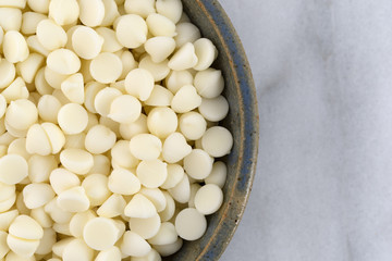 White chocolate baking chips in a bowl atop a gray marble cutting board.