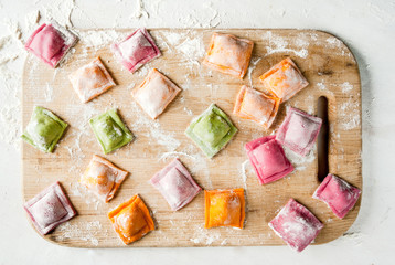Multi-colored ravioli on a cutting board, sprinkled with flour, cooking process, on a white table. Funny food for children. Top view
