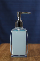 Obraz premium Light blue liquid soap dispenser with a chrome top on a wooden shelf with a dark blue background