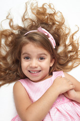girl child with long hair lie on white and open arms, dressed in pink