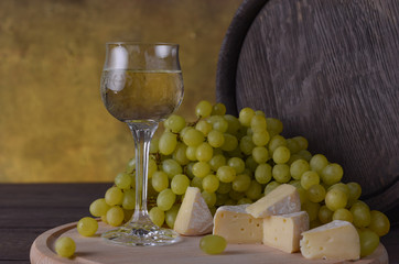 A glass of wine on the background of white grapes, and barrels of cheese on a wooden table