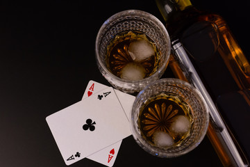 Two galsses of whiskey, a bottle and two aces on black.