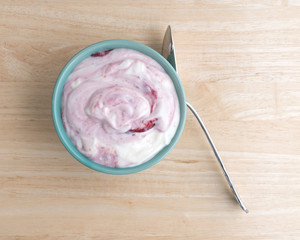 Raspberry yogurt in a bowl on a table with a spoon to the side.