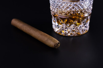A crystal glass of whiskey and a cigar on black