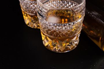 A bottle of whisky and two crystal glasses on black