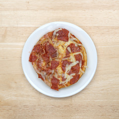 Personal size pepperoni pizza on a white plate top view atop a wood table.