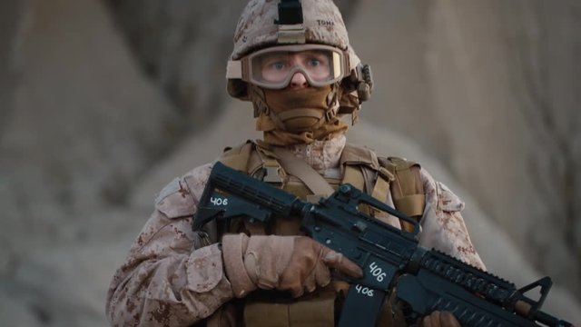 Portrait of Fully Equipped and Armed Soldier Wearing Safety Glasses in Desert Environment