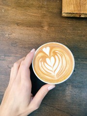 Cup of coffe to take away with heart sign, milk, latte, wooden hipster table