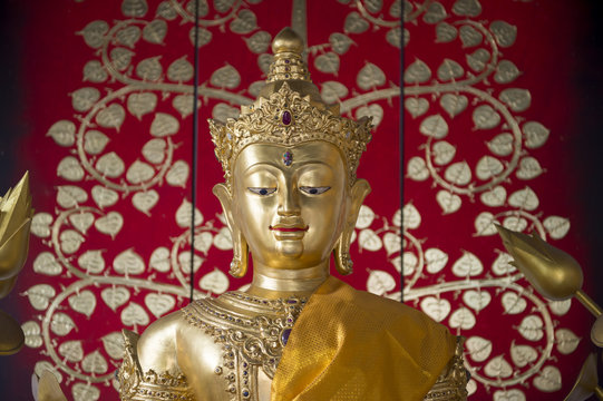 Golden buddha with sash close up against a bright decorative floral patterned background in a Buddhist temple in Bangkok Thailand