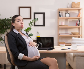 Pregnant business woman practicing uterine contraction while working at home with laptop computer. Young brunette lady touching her belly.