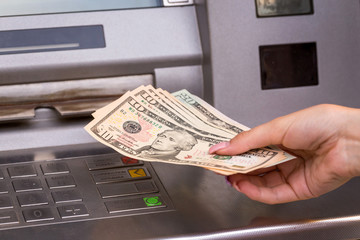 woman hand showing dollar banknotes in front of the atm