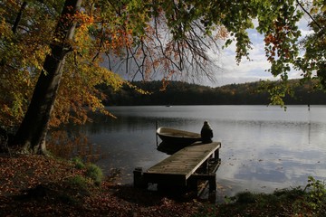 Frau sitzt auf einem Holzsteg am See im Herbst