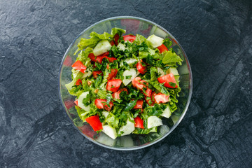 Fresh salad with tomato, cucumber, greens on black marble background. Top view.