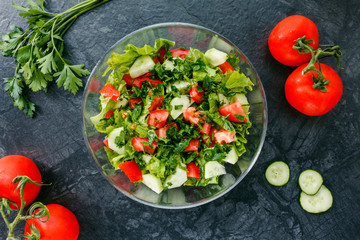Fresh salad with tomato, cucumber, greens on black background. Top view. Healthy food or diet nutrition concept.