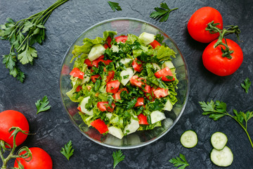 Fresh salad with tomato, cucumber, greens on black background. Top view.