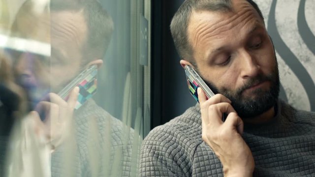 Sad, worried man talking on cellphone sitting by window in cafe
