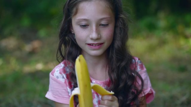 Beautiful little girl eating a banana in the garden