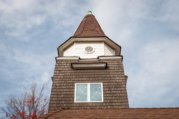 Building steeple roof wood shingle siding wall. Abstract roof design and detail. Architectural detail and design. Abstract colors and design. Cloudy sky background. Minimal architecture design. 
