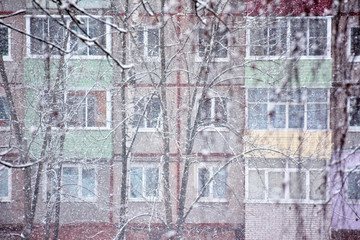 Heavy snowfall opposite windows and balconies on colorful wall of residential house. Shallow depth of field, focus on wall of house