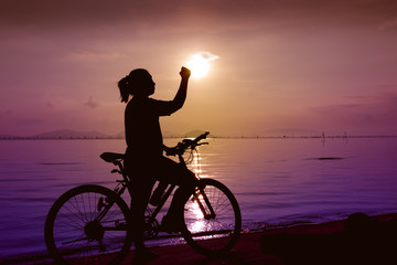 Fototapeta premium Silhouette of happy female celebrating with arm up towards the sun