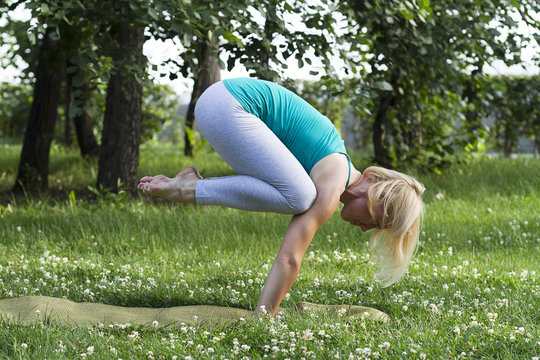  Young flexible woman doing yoga on the grass, pose a crane,
 bakasana