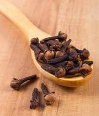 Heap of cloves with wooden spoon on table, seasoning for cooking