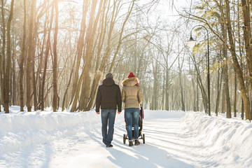Fototapeta na wymiar Father and mother with baby carriage in winter forest