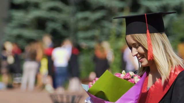 Happy female graduate laughing with bouquet of flowers in hands, celebration