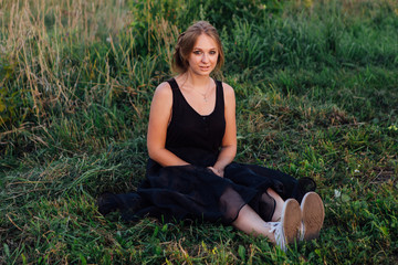 Slim girl in black dress in the field at sunset