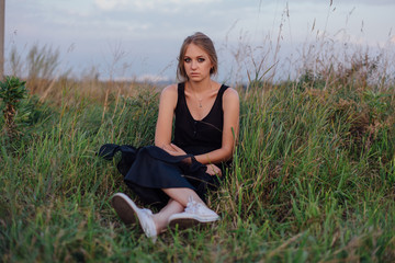 Slim girl in black dress in the field at sunset